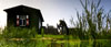 Man sitting at a barn, reflected in water